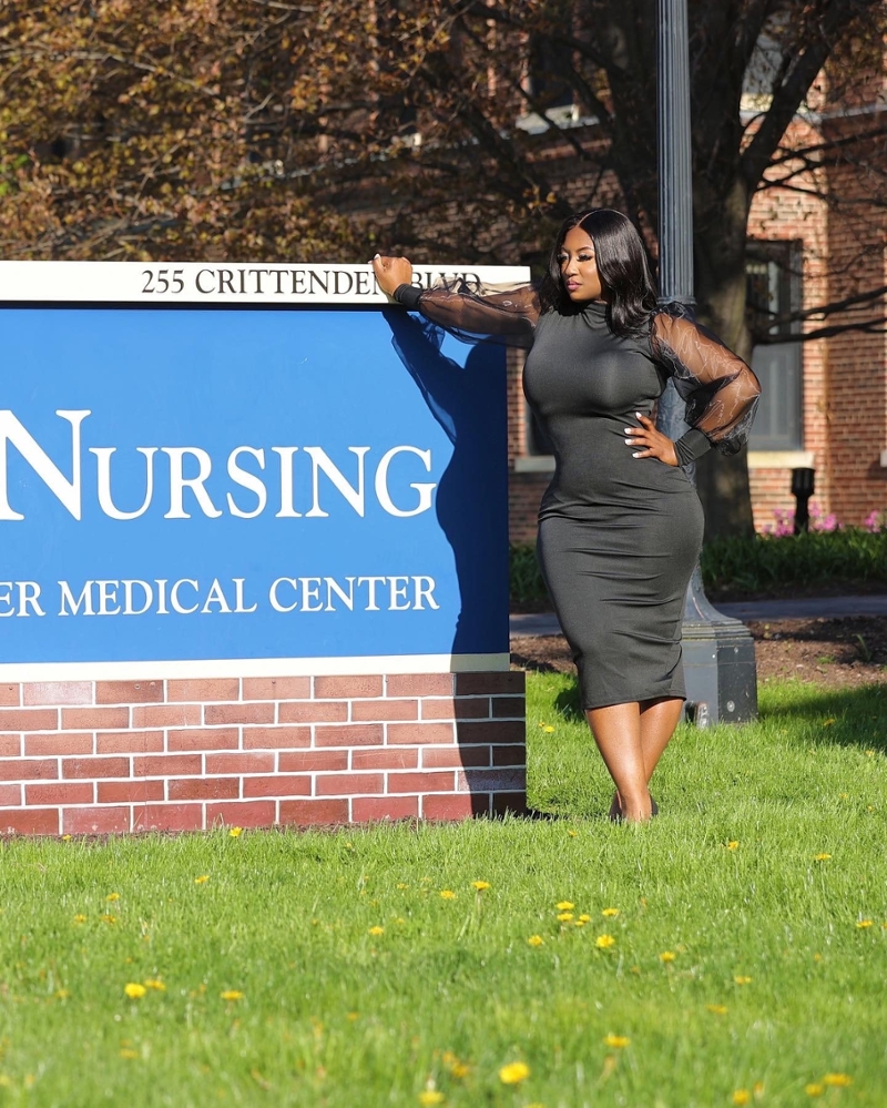 Natalie Lewis standing in front of the sign for the School of Nursing, wearing a black dress.