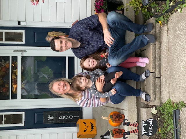 Family photo of Melissa, her husband and two daughters on a front porch, surrounded by Halloween decoratins.