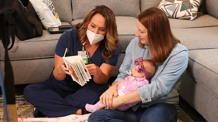 A nurse in blue scrubs visits a mother and baby at home.