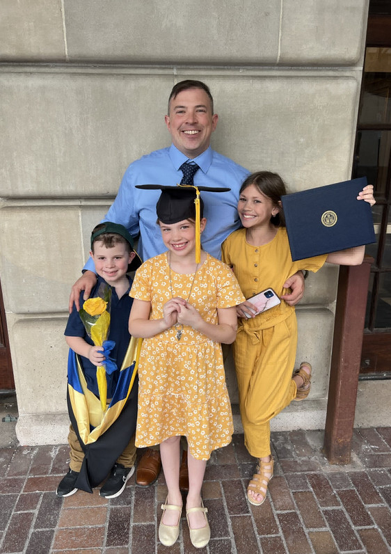 Joseph Escobar takes a graduation photo with his 3 children, who are holding his cap, stole, and diploma