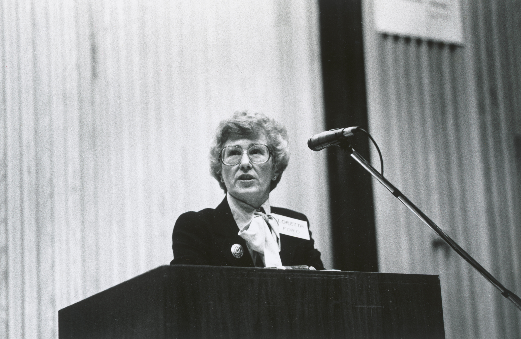 Black and white photo of Loretta Ford speaking at a podium.