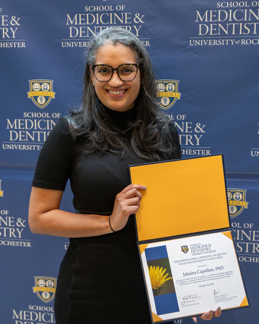 Jahaira Capellan stands in front of a blue School of Medicine backdrop.