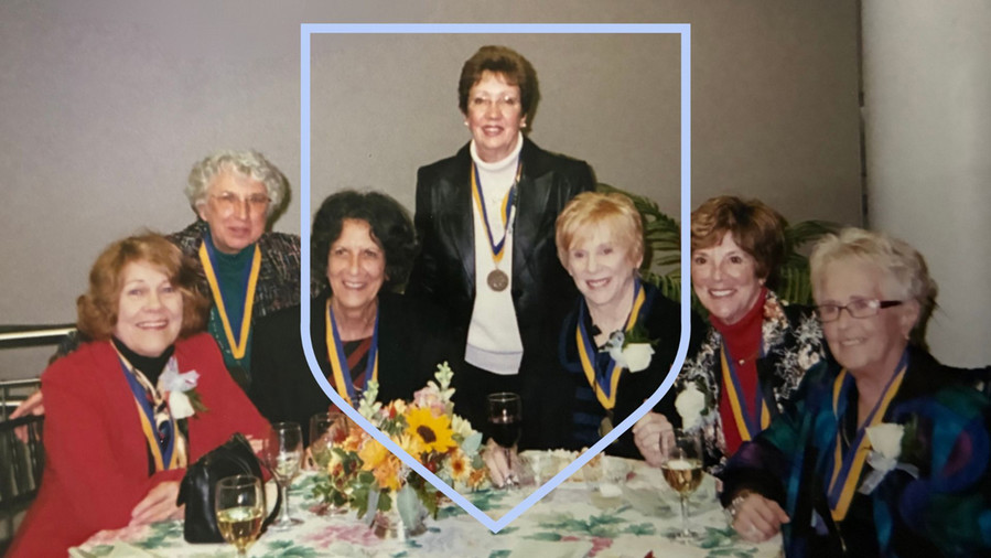 Scanned photo of a group of women at a dinner table, wearing matching gold medals.