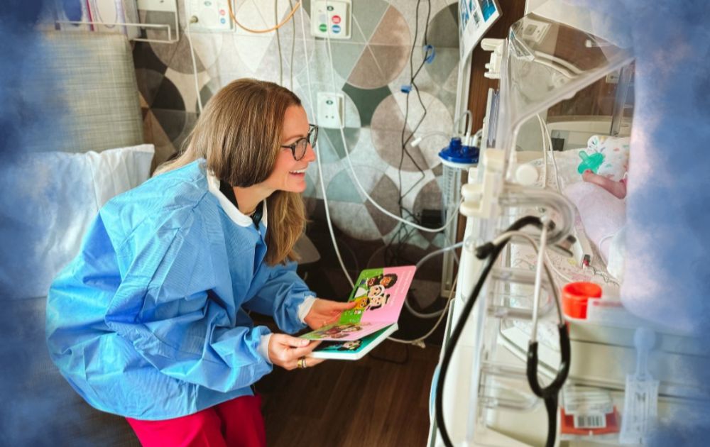 Meghan Aldrich reads a children's book to a baby in a hospital room.