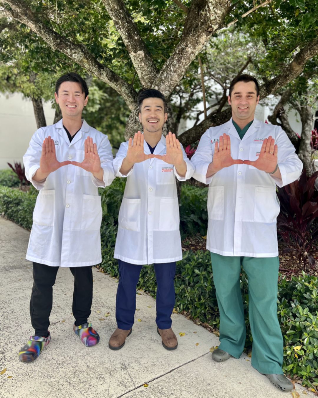 Mark and two colleagues smile in an outdoor photo, wearing white coats.